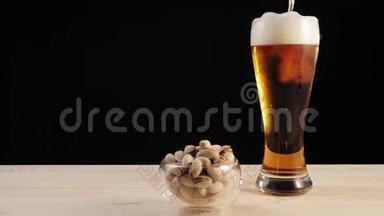 新鲜啤酒。 啤酒杯中的美味啤酒，靠近开心果碟，放在黑色背景的木桌上